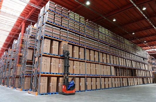 the middle photo shows a a warehouse with racking system. many big packages are stored on the racking system. An operator with a for-lift is in the middle of taking one big package of refrigerator from the rack. 